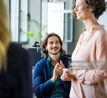 Smiling young businessman applauding while looking at female entrepreneur during presentation in meeting